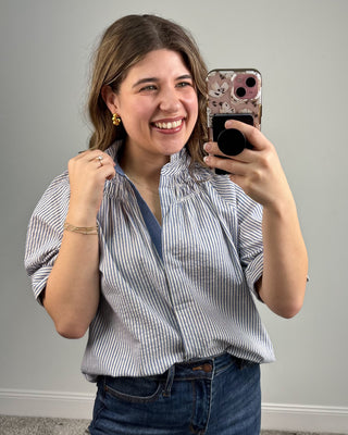 Woman taking a mirror selfie with a phone, wearing a striped shirt and jeans.