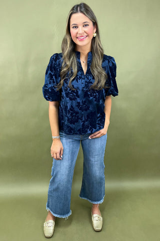 Woman wearing a blue velvet top and jeans on a green background