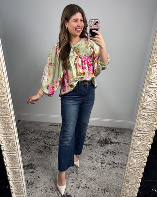 Woman taking a mirror selfie wearing a floral blouse and blue jeans.