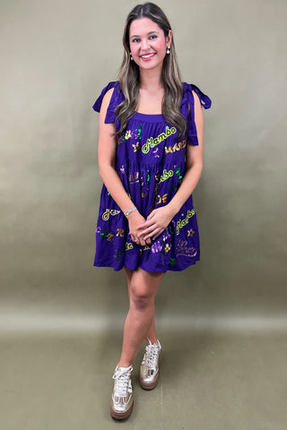 Woman wearing a purple dress with colorful patterns against a plain background