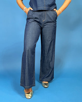 A person wearing dark blue wide-leg denim jeans with a matching top, standing against a solid blue studio background.