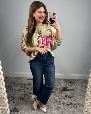 Woman taking a mirror selfie wearing a floral blouse and jeans.