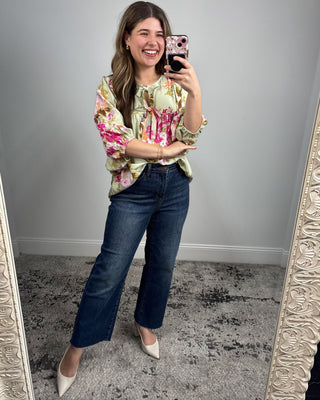 Woman taking a mirror selfie wearing a floral blouse and blue jeans.