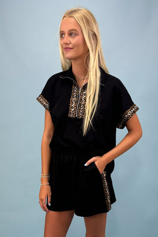 Woman wearing a black outfit with leopard print accents against a light blue background