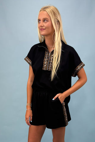 Woman wearing a black outfit with leopard print accents against a light blue background