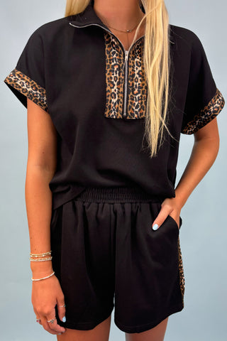 Person wearing a black outfit with leopard print accents on a plain background