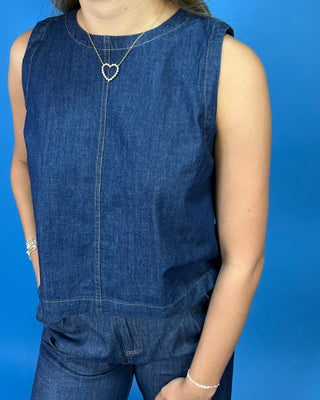 The top has a straight neckline, front seam, and relaxed fit, with visible gold jewelry including a heart-shaped pendant necklace and bracelets.