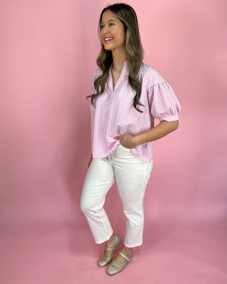 Woman wearing a pink and white striped blouse and white pants against a pink background