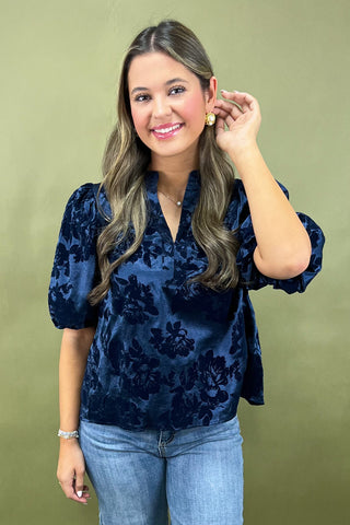 Woman wearing a navy floral blouse and blue jeans against a green background