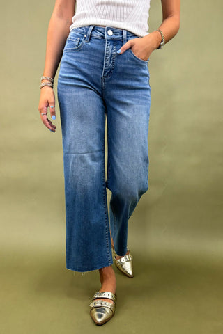Person wearing blue jeans and silver shoes on a green background