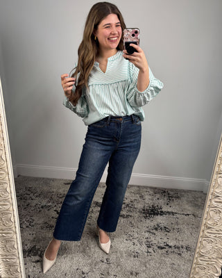 Woman taking a mirror selfie wearing a striped blouse and jeans.
