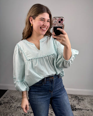 Woman taking a mirror selfie wearing a striped blouse and jeans.