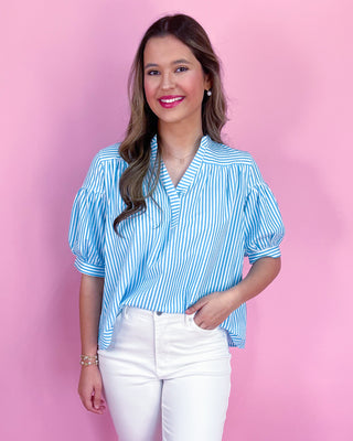 Woman wearing a blue striped shirt and white pants against a pink background