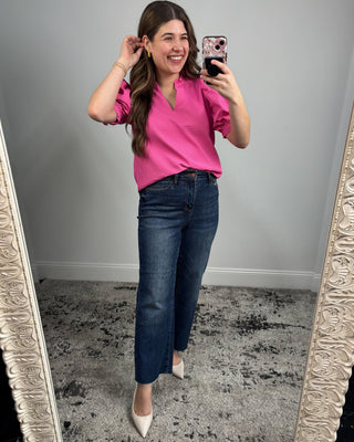 Woman taking a mirror selfie wearing a pink top and blue jeans.