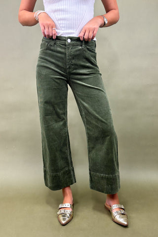 Person wearing green corduroy pants and silver shoes on a plain background