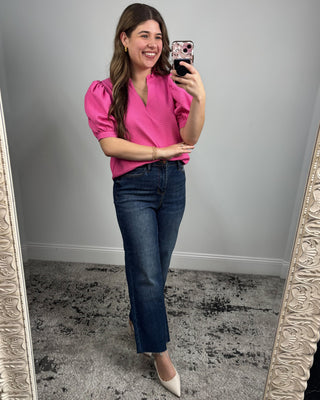 Woman taking a mirror selfie wearing a pink top and blue jeans.