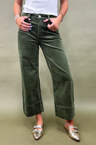 Person wearing green wide-leg pants and silver shoes on a plain background
