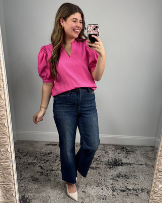 Woman taking a mirror selfie wearing a pink top and blue jeans.