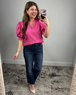 Woman taking a mirror selfie wearing a pink top and blue jeans.