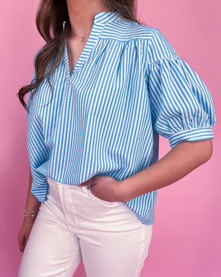Person wearing a blue and white striped shirt with white pants against a pink background