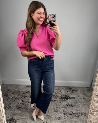 Woman taking a mirror selfie wearing a pink top and blue jeans.
