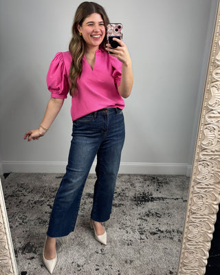 Woman taking a mirror selfie wearing a pink top and blue jeans.