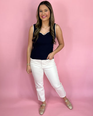 Woman wearing a navy top and white pants against a pink background