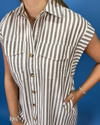 A close-up of a woman wearing a short-sleeve button-front shirt dress with vertical brown and off-white stripes, set against a solid blue background.