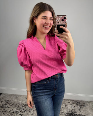 Woman taking a mirror selfie wearing a pink blouse and blue jeans.