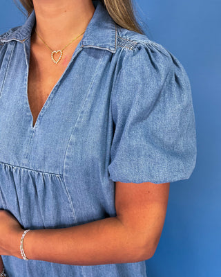 Woman wearing a blue denim dress with puff sleeves against a blue background