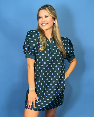 A woman modeling a dark green short-sleeve mini dress with a light blue polka dot pattern