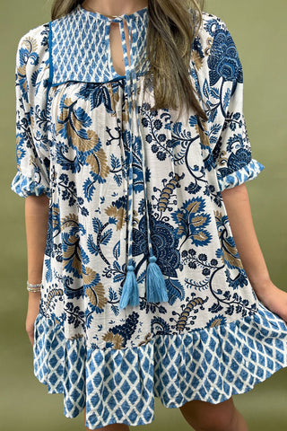 Woman wearing a blue and white patterned dress with tassels on a green background