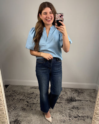 Woman taking a mirror selfie wearing a blue top and dark jeans.