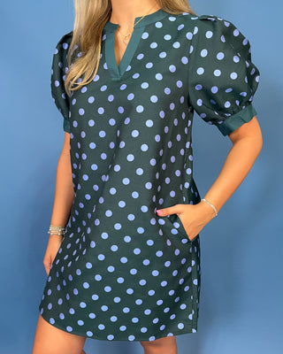 A woman wearing a dark green puff-sleeve mini dress with a light blue polka dot pattern