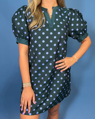 A woman wearing a dark green puff-sleeve mini dress with light blue polka dots