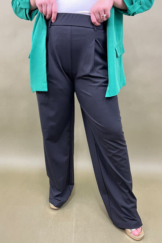 Person wearing black pants with a green jacket on a beige background
