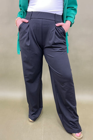 Person wearing dark gray pants with a green jacket on a beige background