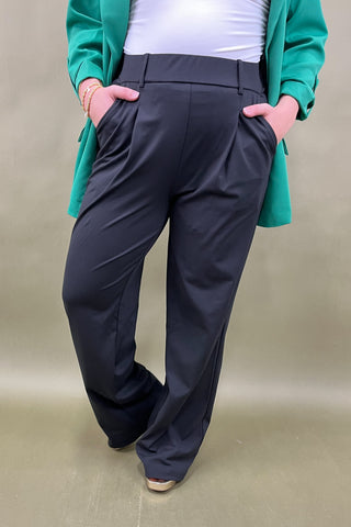 Person wearing black pants with a green cardigan on a beige background