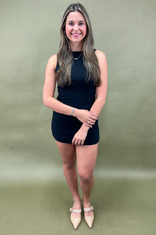 Sleek black sleeveless bodycon mini dress styled with beige pointed-toe heels and simple gold jewelry