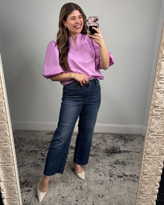 Woman taking a mirror selfie wearing a pink blouse and blue jeans.