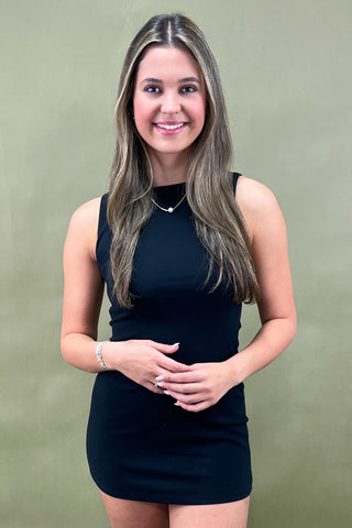 Sleek black sleeveless bodycon mini dress styled with beige pointed-toe heels and simple gold jewelry