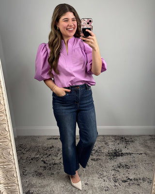 Woman taking a mirror selfie wearing a purple blouse and blue jeans.