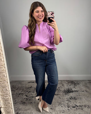 Woman taking a mirror selfie wearing a purple blouse and blue jeans.