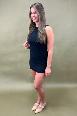 Sleek black sleeveless bodycon mini dress styled with beige pointed-toe heels and simple gold jewelry