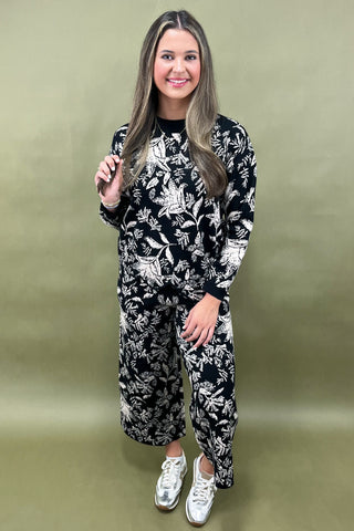 Woman wearing a black and white floral jumpsuit against a green background