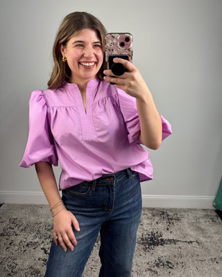 Woman taking a mirror selfie wearing a purple blouse and blue jeans.