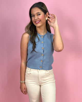 Woman wearing a blue sleeveless cardigan against a pink background