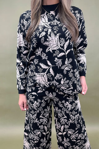 Person wearing a black and white floral patterned outfit on a plain background