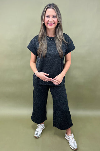 Woman wearing a dark gray outfit with white sneakers on a green background