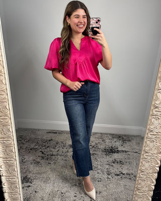 Woman taking a mirror selfie wearing a pink top and blue jeans.